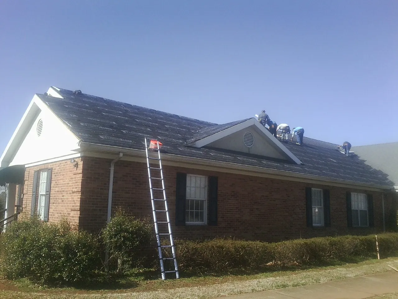 Crew tearing shingles off a brick ranch roof with a ladder set — Emergency Roof Repair work by our crew in Tybee Island