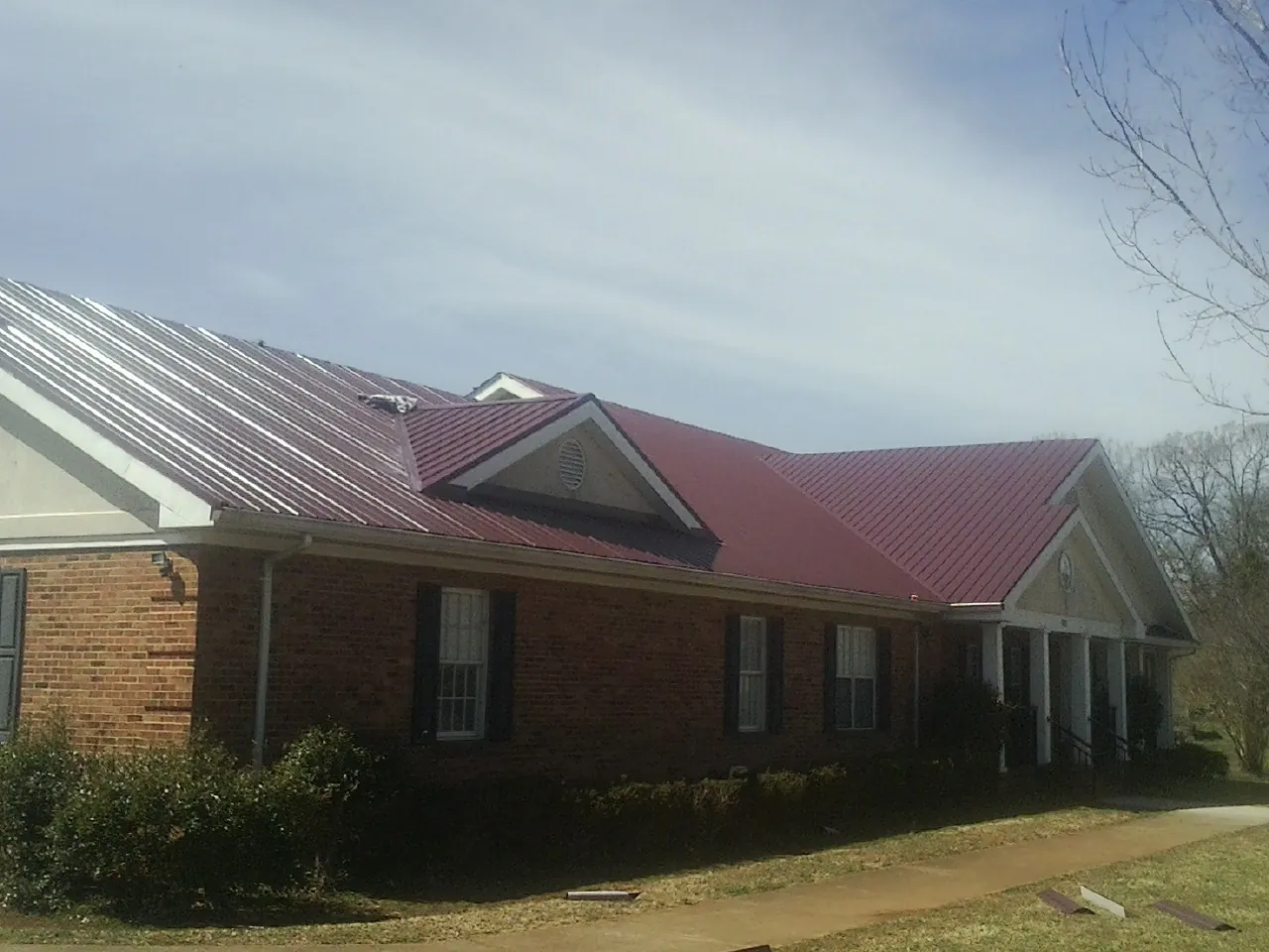 Red metal roof with gabled entries on a long brick building, from a Hail Damage Roof Repair job in Tybee Island