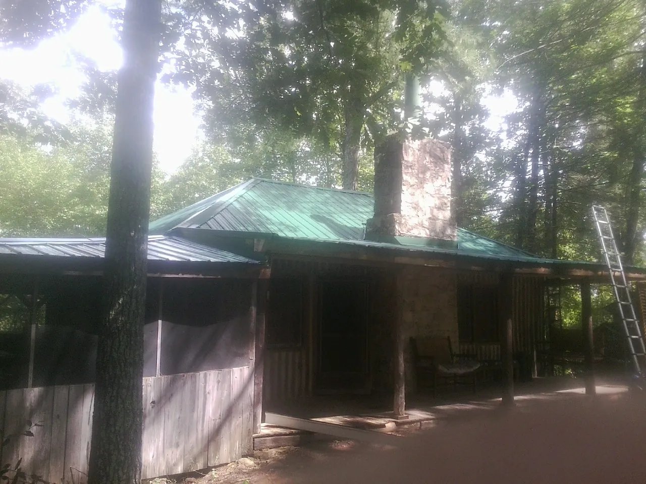 Green metal roof and stone chimney above a log cabin porch in Tybee Island