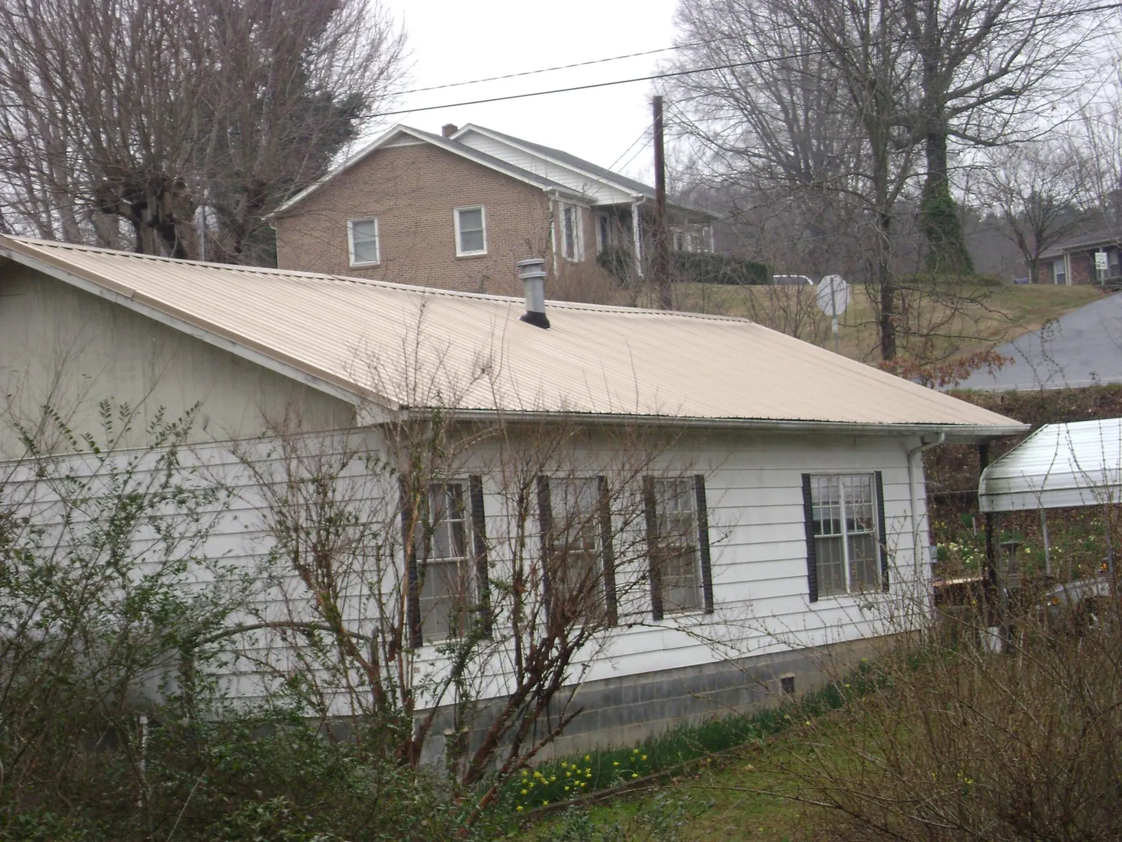 Tan metal roof on a white sided house set into a hillside — Commercial Roofing by Roofing Brothers in Tybee Island